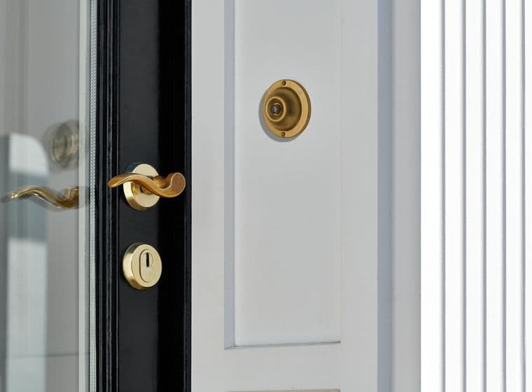 Close-up of a white door with a black frame, featuring a gold handle, lock, and doorbell.