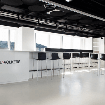 Engel & Völkers office interior with a white counter, black stools, and large windows with a mountain view.