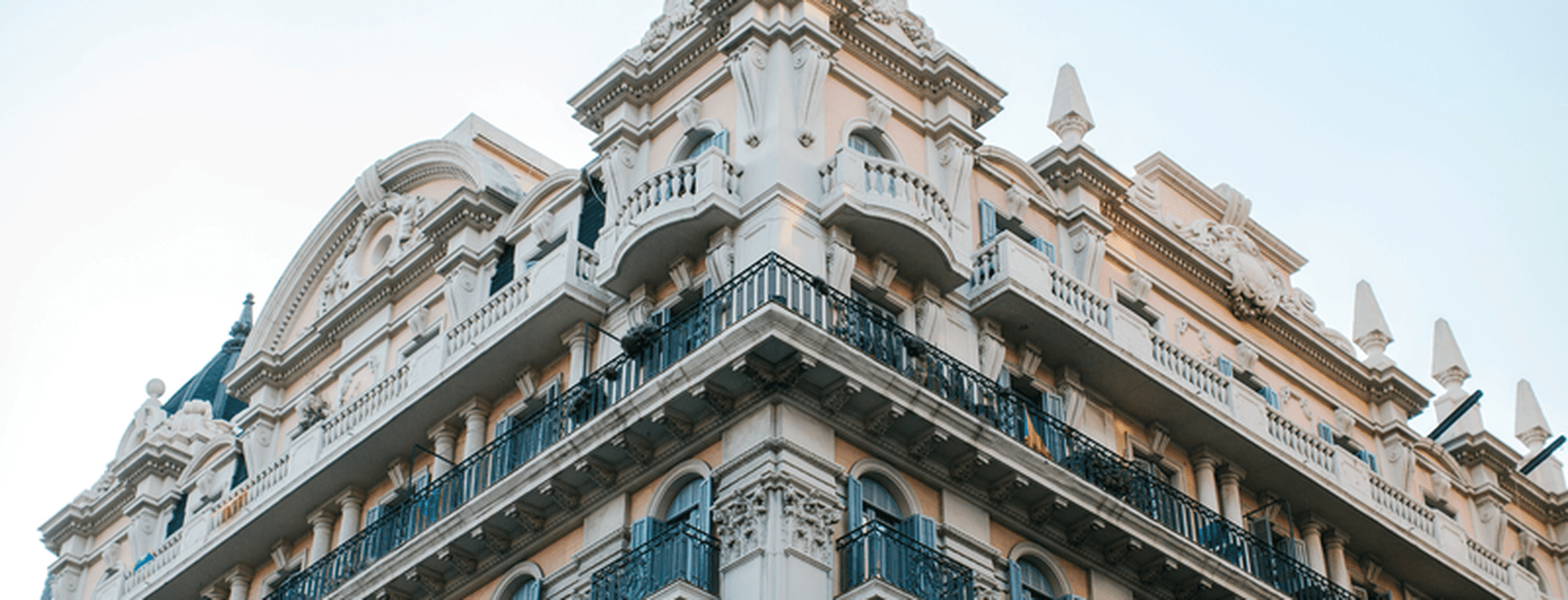 Ornate multi-story building with decorative balconies, intricate architectural details, and a pointed roof against a clear blue sky.