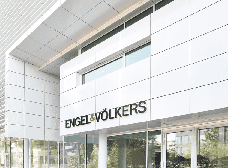 Exterior of Engel & Völkers office building. White facade with black logo above glass doors.