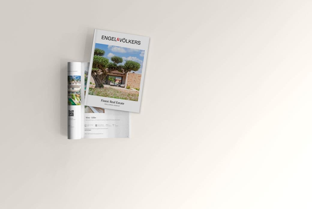 Angled Engel & Völkers real estate brochure atop an open magazine on a pale beige background, cover photo of an olive tree and Mediterranean villa.