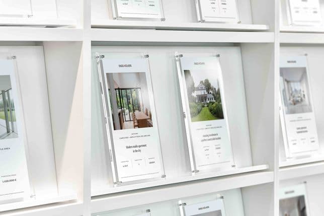 Real estate flyers on a white shelf. Flyers advertise a modern studio apartment and a townhouse with prices and details.