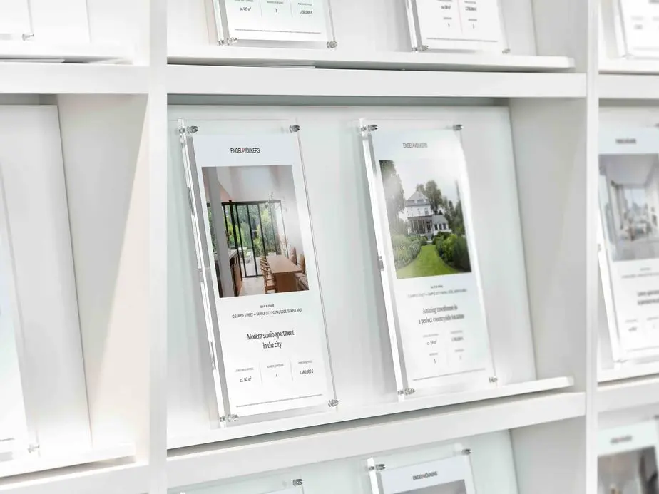 Modern display wall featuring multiple acrylic property listing cards mounted in an organized grid. Each display case contains property photos and details with clear glass or acrylic holders against a clean white wall, creating a professional showcase of available properties.