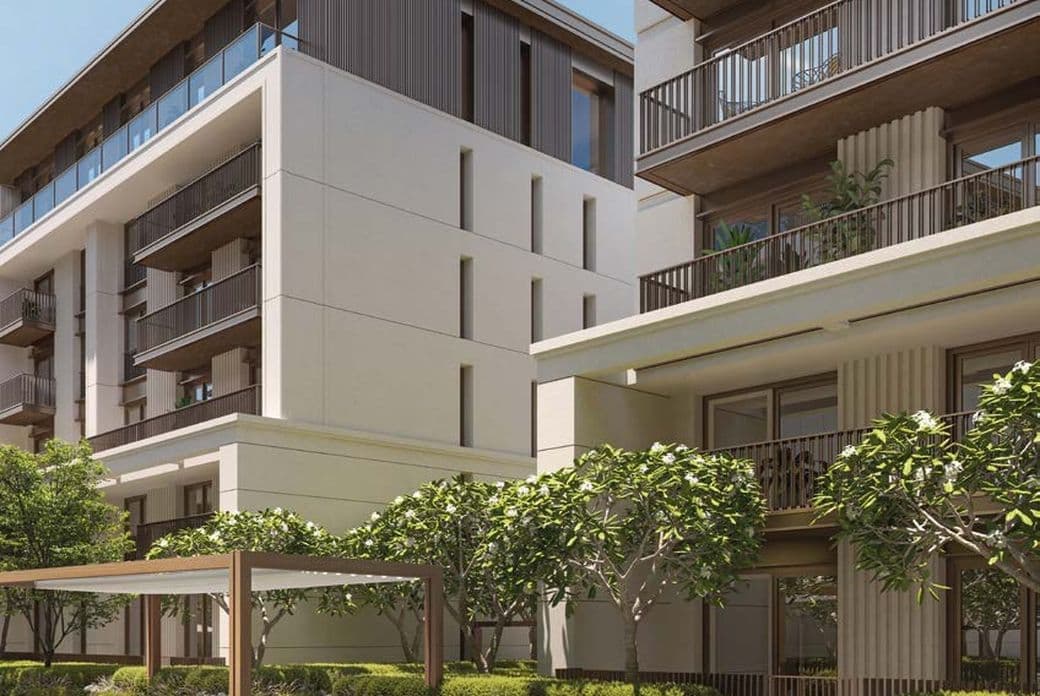 Modern apartment buildings with balconies, surrounded by landscaped greenery and trees, under a clear blue sky.
