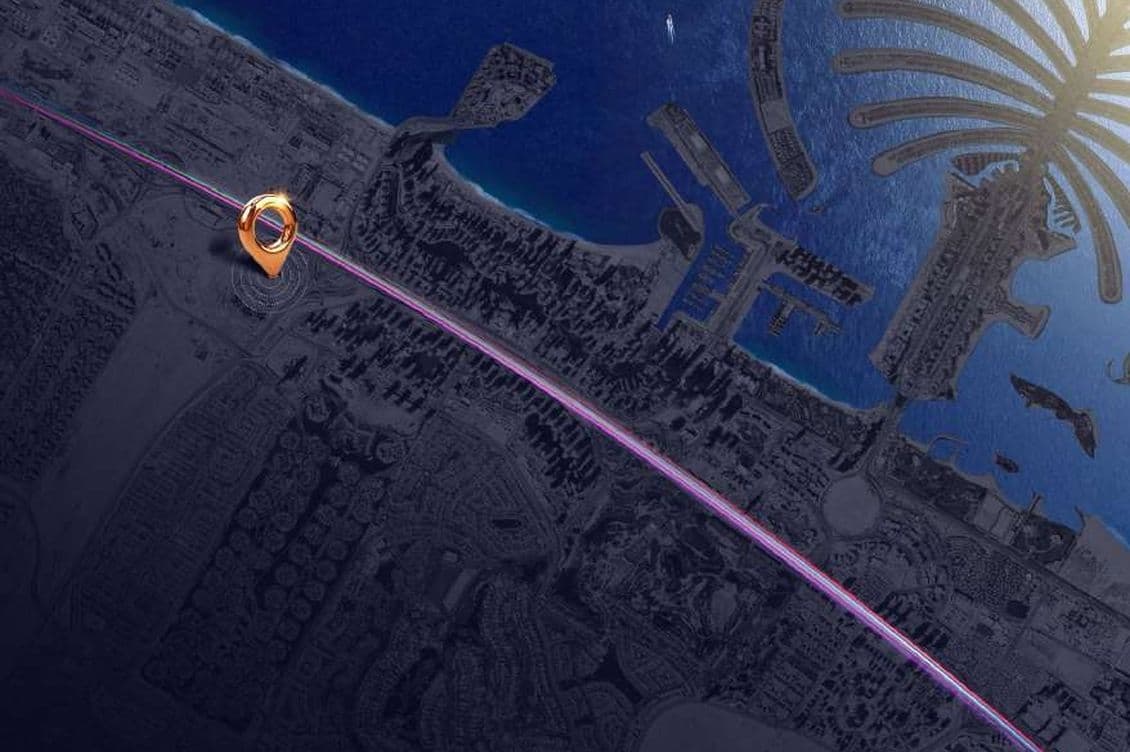 Aerial view of an urban coastline with a futuristic ringed structure and illuminated pathways by the sea. Palm-shaped land formation visible.