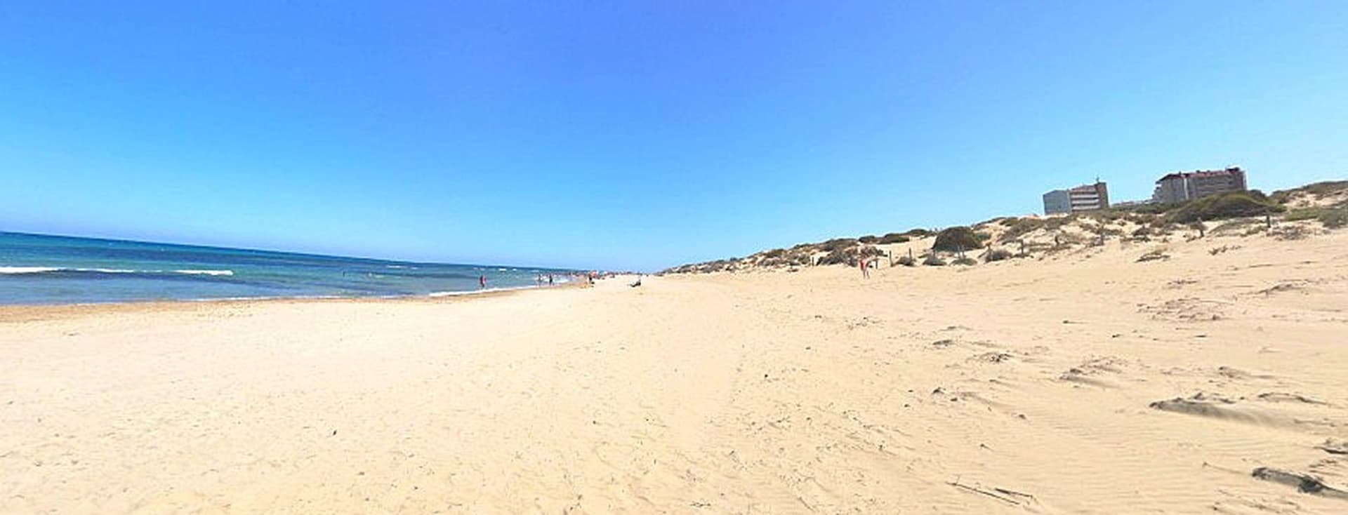 Vista de la Platja Les Ortigues Torrevella amb la seva sorra blanca i el mar a l'horitzó.