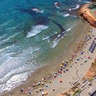 Panoramic view of Playa flamenca beach with parasol and tennis court and pools by a hotel on the top right hand corner of the picture