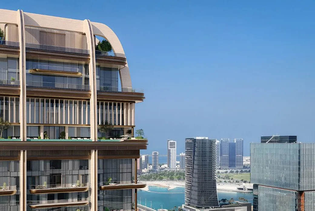 A modern high-rise with curved arches and balconies on the left, overlooking a coastal city skyline and blue sky.