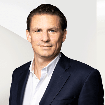 Sebastian König in einem dunklen Anzug und einem weißen Hemd, der vor einem hellen Hintergrund steht.