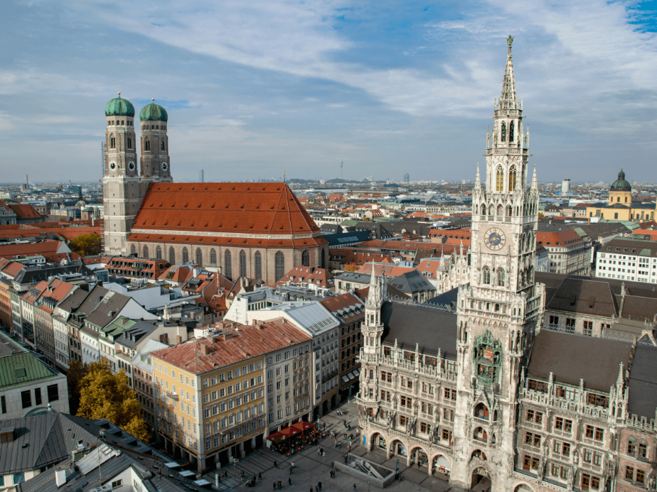 Aerial view of Munich's Marienplatz with the New Town Hall and Frauenkirche, surrounded by historic buildings under a cloudy sky.