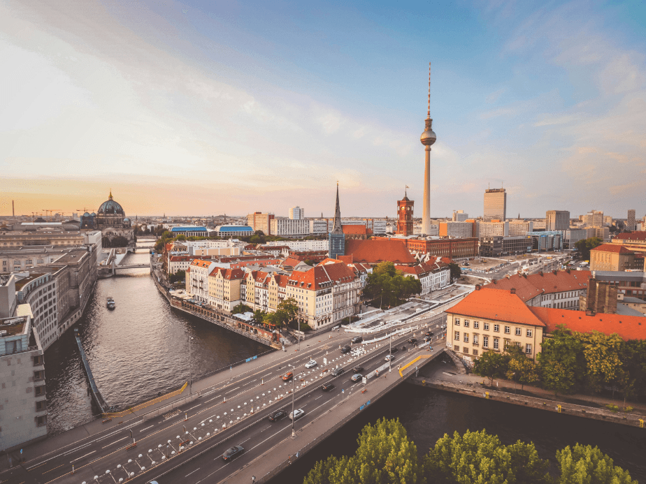Aerial view of Berlin with the TV Tower, river, and historic buildings under a clear sky at sunset.
