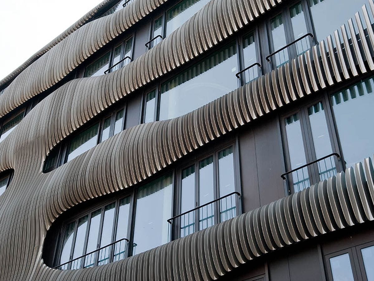 A modern building facade with undulating, wave-like, wooden slats covering glass windows and balconies.