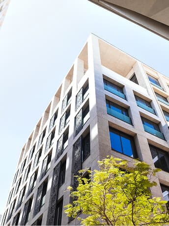 Ein modernes Wohnzimmer mit hohen Decken, freiliegenden Holzbalken, großen Fenstern, weißen Wänden und einem farblich neutralen Sofa mit Kissen. Im Hintergrund befindet sich eine Treppe, die in die obere Etage führt.